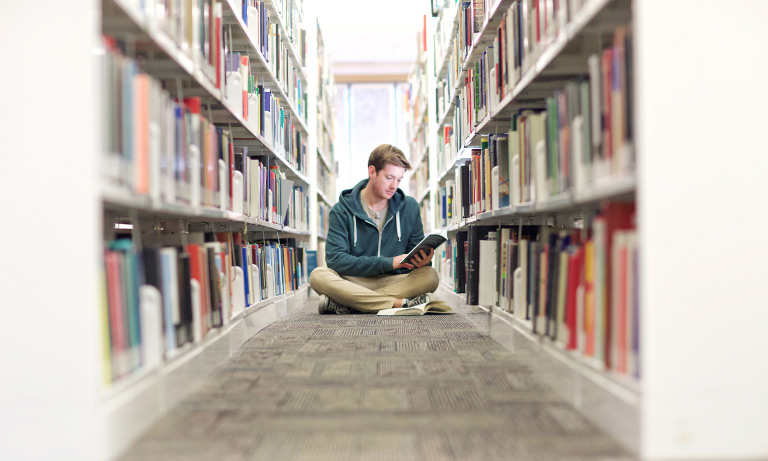 student reading between rows of bookshelves